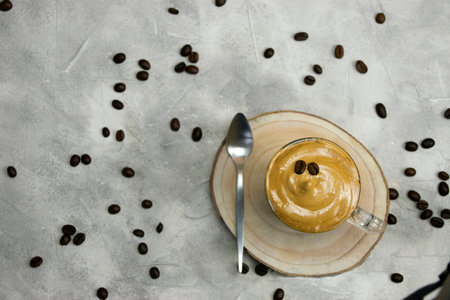 Top view of whipped instant coffee con a crystal mug with a spoon on a wooden coaster on a grey...