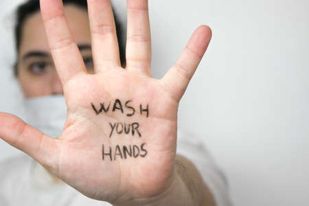 Woman on a side wearing a safety mask with hand opened with the sentence "wash your hands" written on the palm of her hand on a white background. Coronavirus concept.の写真素材
