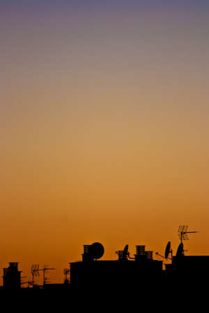 Contrast buildings and antennas at orange sunset skyの写真素材