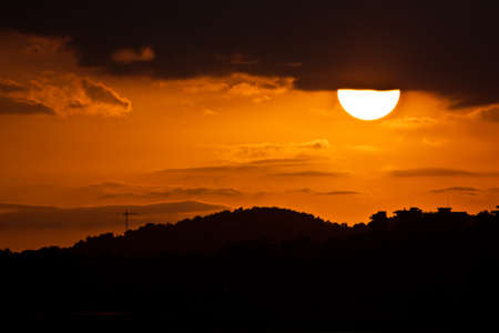 Sunset landscape, half sun and observed under a mountainの写真素材
