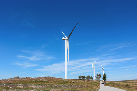 Several wind turbines in rocky and deserted landscape with few trees, against beautiful clear blue...