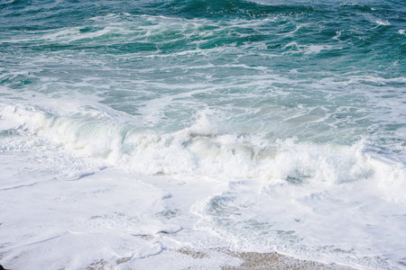 Horizontal photo of turquoise ocean water with small white foam waves gently crashing into golden...
