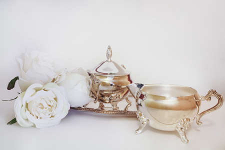 Antique silver creamer and sugar set and decorative white flowers in white background. Afternoon tea concept.の写真素材