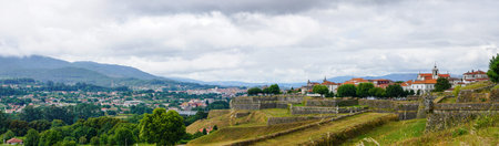 A panoramic view of a small town in the mountains with a stone wall in the foreground. The scene...