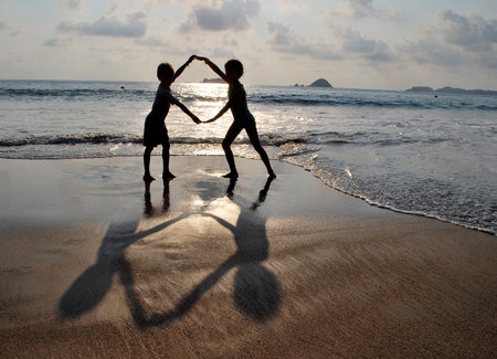 Contrasting silhouette of boy and girl holding hands at the beachの写真素材