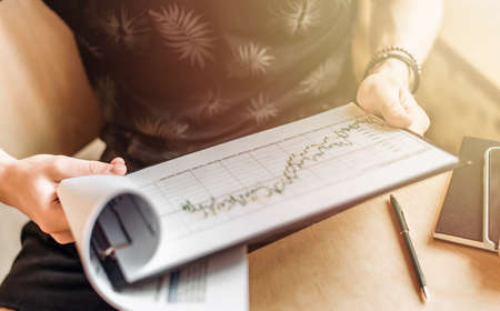 A closeup photo of a man holding a financial chart in his hands and looking at it. The concept of business growth and finance. Risk assessment. Stock growth chart.の写真素材