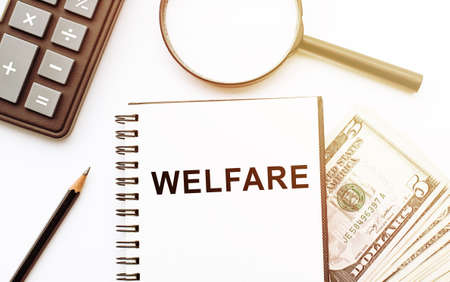 The word WELFARE written on notebook on table with calculatir, magnifier, pencil and dollarsの写真素材