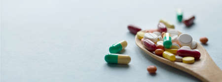 pharmaceutical medicine pills, tablets and capsules in a wooden spoon on a blue table. Medical and health concept. Closeup for your designの写真素材
