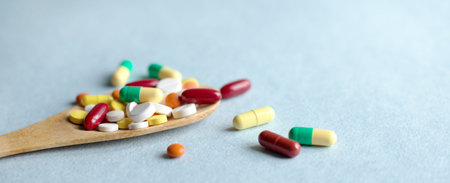 pharmaceutical medicine pills, tablets and capsules in a wooden spoon on a blue table. Medical and...