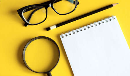 Business concept with notebook, magnifier and black glasses on yellow backgroundの写真素材