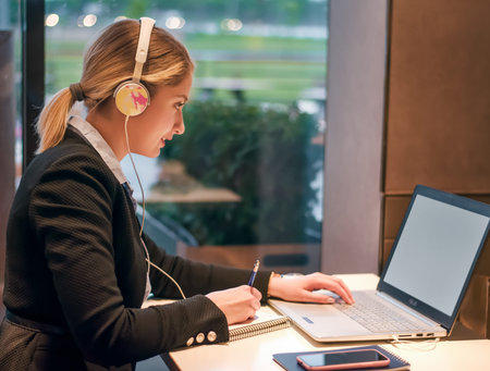 Happy young girl with headphones looking at laptop screen and smiling, reading listening online...