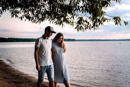 Happy pregnant family walks along the lake in summerの写真素材