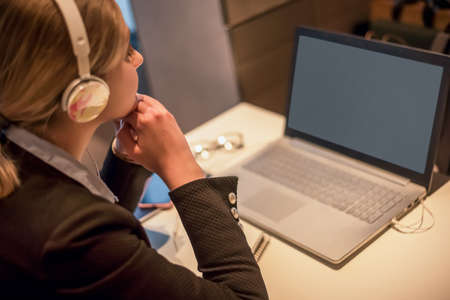 Happy young girl with headphones looking at laptop screen, reading listening online courses, studying or working remotelyの写真素材