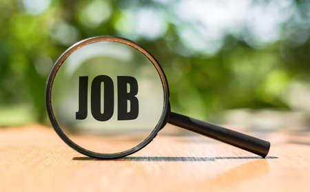 magnifying glass with text JOB on wooden table and green background. Business and job search concept imageの写真素材