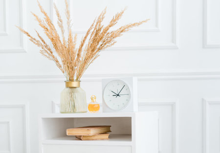 Modern light interior with vintage coffee table with flowers, clock books and perfume bottle on it.