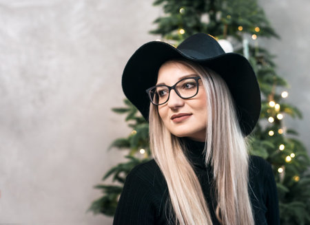 Young beautiful woman in a black hat on the background of the Christmas tree.