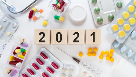 2021 text on wooden blocks on a desk. Medical concept with pills, vitamins, stethoscope and syringe on the background.の写真素材