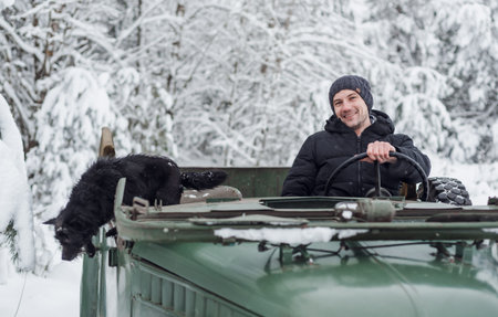 Minsk, Belarus - January 09, 2021: Young smiling man driving a vintage car with her dog in winter...