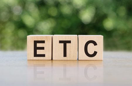 ETC (abbreviation of et cetera) word written on wooden blocks. The text is written in black letters and is reflected in the mirror surface of the table.の写真素材