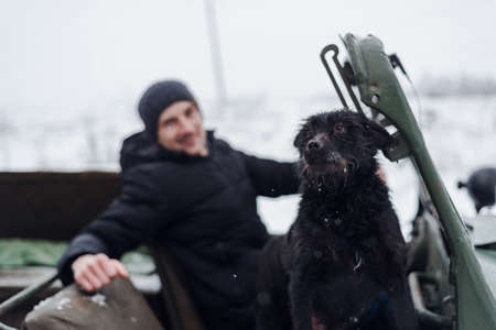 Minsk, Belarus - January 09, 2021: Young man driving together with his dog on vintage car in winter forestのeditorial素材