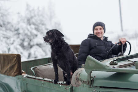 Minsk, Belarus - January 09, 2021: Smiling man traveling in winter forest with his dog on vintage carのeditorial素材