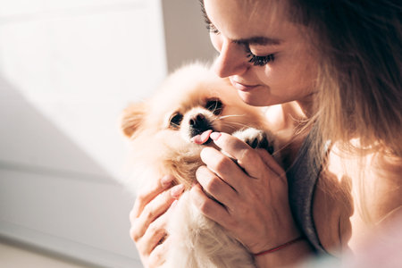 A young girl holds in her arms her beautiful happy dog and looks at himの写真素材
