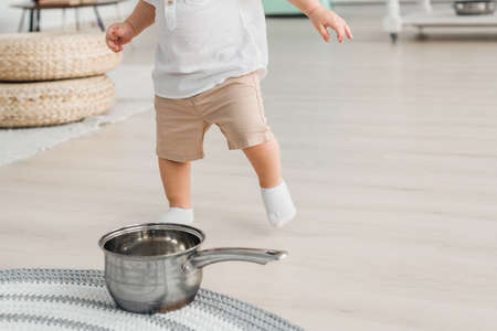 The baby boy runs to the pan, which stands on the floor. The child plays with kitchen utensilsの写真素材