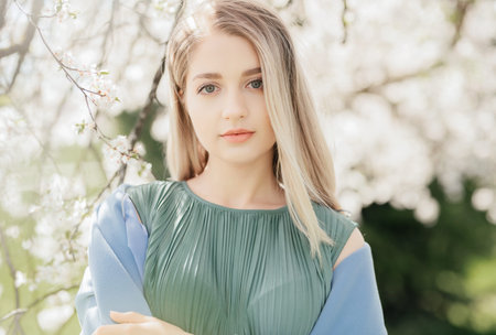 Outdoors fashion photo of beautiful young lady in the garden of apple blossoms