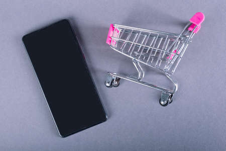 Trolley and black smartphone isolated on gray background. Shopping online concept.の写真素材