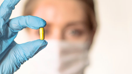 Doctor holding a pill, looking at it and giving it as a treatment to the patientの写真素材
