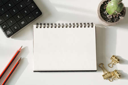 Top view open notebook, calculator, pencil and plant potted on white desk backgroundの写真素材