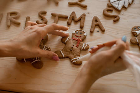 Gingerbread man in the making. Woman cooking on wooden table. Inscription from baking a merry Christmasの写真素材