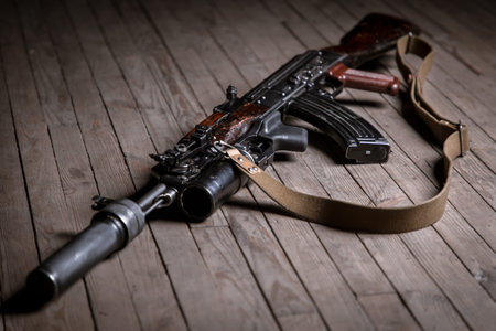 Close up of isolated assault rifle with suppressor on wooden background