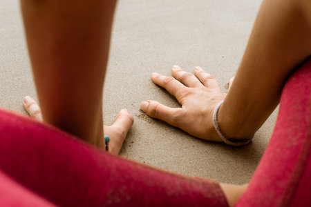 Close up of a woman sitting on a mat at the beach practicing yoga. Woman sitting at the beach in a...