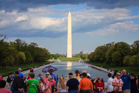 Sun illuminating the Washington monument through a hole in the clouds while the surrounding area is in the shade. Group of tourists looking from Lincoln memorial across reflecting pool, Washington DCのeditorial素材