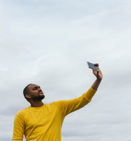 Young black man taking a selfie and smiling at the cameraの写真素材
