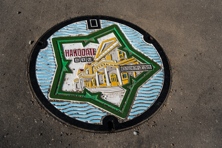 Manhole cover of Hakodate with two of the city's symbol: the star-shaped Goryukaku and the old public hall of Hakodateの写真素材