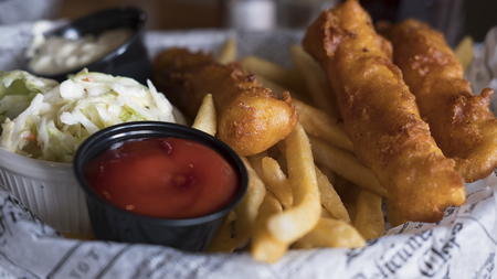 Close-up shot of a tasty plate of fish and chips, coleslaw and salsas served in English style on a plate covered with newspaper cuts, on Santa Monica pier, Los Angeles, Californiaの写真素材