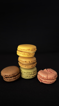 Assortment of traditional French macaroons, selection of different colors and flavors, very light bite-size confectionery, with one raspberry macaron crushed, with black background and selective focusの写真素材