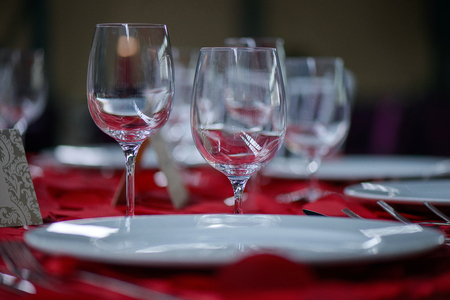 Fine dining table setting with white china and wine and water crystal glasses, with silverware in the order of use, and romantic red tablecloth ready for guests at an event, wedding or at a restaurantの写真素材