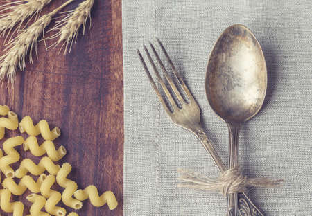 Closeup of vintage fork and spoon laying at the table with pasta and ears of wheat. Retro toned picture.の写真素材