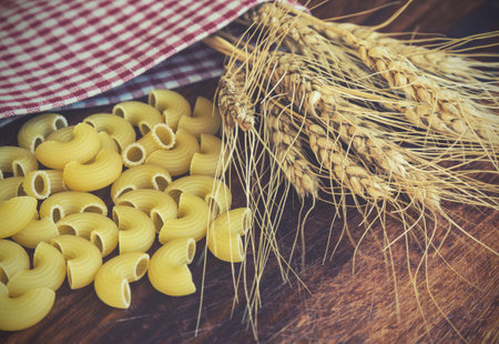 Vintage toned picture of the ears of wheat with pasta on the wooden background.の写真素材