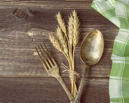 Vintage toned picture of the fork and spoon with the ears of wheat lying at the old table.の写真素材