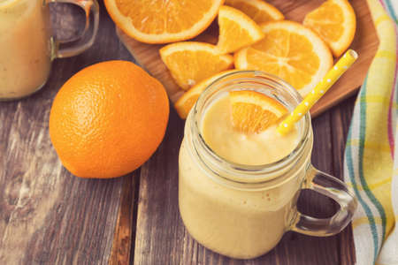 Orange fruit smoothie in the glass jar with fresh orange slices on rustic wooden backgroundの写真素材