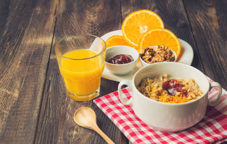 Oatmeal with walnuts, orange peel and jam for breakfast on rustic wooden backgroundの写真素材