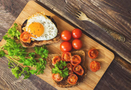 Toasts with egg and fried tomatoes on rustic wooden background. Healthy breakfast.の写真素材