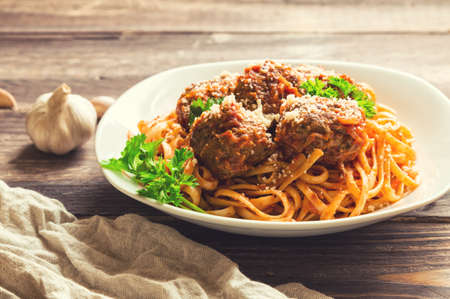 Linguine pasta with meatballs in tomato sauce and parsley on rustic wooden background. Selective focus.の写真素材