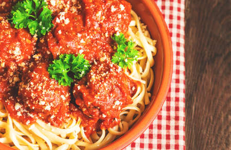 Linguine pasta with meatballs in tomato sauce and parsley in clay bowl on rustic wooden background. Top view.の写真素材