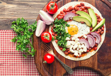 Huevos rancheros breakfast pizza with tomatoes, onion and parsley on rustic wooden background. Top view.の写真素材