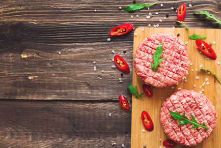 Raw ground beef burgers with chili pepper and arugula on rustic wooden background. Top view.の写真素材